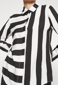 Randig skjorta i svart och vitt med krage och knäppning, med varierande bredd på ränderna och en mjuk, slät textur.