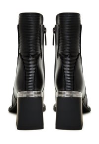 Bottines noires avec un extérieur en cuir côtelé, fermeture éclair et un accent métallique argenté sur le talon bloc. Semelle lisse noire.
