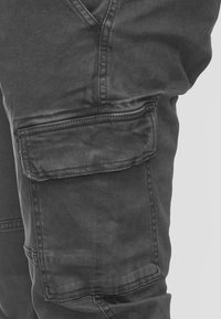 Pantaloni cargo neri in denim, con tasca laterale, dettagli cuciti e superficie leggermente testurizzata, ideali per un look casual.