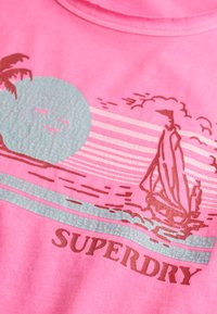 Roze stof met vervaarde afdruk van een zeilboot op het water, een zon, vogels, een palmboom, en de tekst "SUPERDRY" eronder.