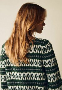 Stickad tröja med ett geometriskt mönster i grönt, vitt och grått. Rund hals, långa ärmar och en avslappnad passform, med textilstruktur.