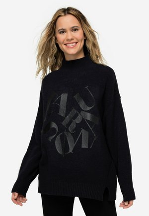Übergrößter schwarzer Strickpullover mit hohem Kragen, der auf der Vorderseite einen strukturierten grafischen Druck von Buchstaben in glänzender Optik zeigt.