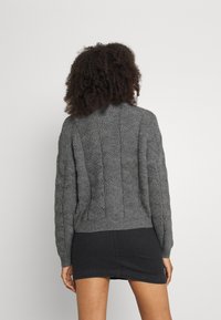 Pull gris en maille torsadée avec encolure ronde et ourlet côtelé. Présente des motifs texturés au dos et des manches longues.