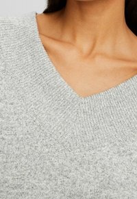 Maglione grigio a maglia con scollatura a V, tessuto strutturato e collo a coste. Materiale morbido con un aspetto leggermente maculato.