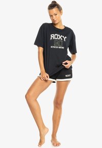 Black oversized t-shirt with white and green graphic print, paired with matching black shorts featuring white trim and logo.