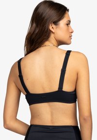 Top bikini nero a coste con spalline regolabili, caratterizzato da una texture liscia e un sottile dettaglio del logo sul retro.