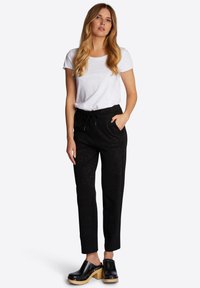 Zwarte broeken met een patroon, een elastische tailleband en koord, gecombineerd met een wit shirt met korte mouwen en zwarte klompen met houten zolen.