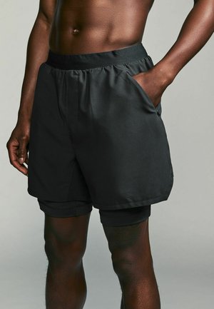 Pantaloni sportivi neri con fodera interna, vita elastica e tasche laterali. Texture liscia con un design funzionale.