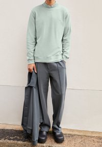 Mintunvihreä, pyöreäkauluksinen collegepaita yhdistettynä harmaisiin laskostettuihin housuihin. Asussa on rento istuvuus ja minimalistinen muotoilu. Mustat paksupohjaiset kengät.