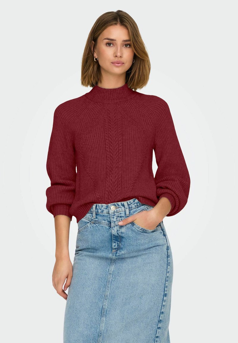 Bordeaux gebreide trui met hoge kraag en ribbeltextuur, gecombineerd met een lichtblauwe denimrok. De trui heeft een kabelbrei ontwerp.