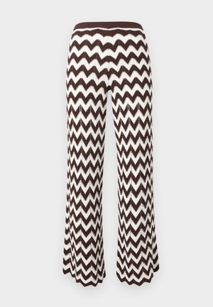 Pantalon tricoté marron et blanc à motif zigzag, avec jambes légèrement évasées et ceinture côtelée sur un fond uni.
