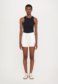 Top negro sin mangas combinado con pantalones cortos blancos que cuentan con una cintura elástica y cordón ajustable, complementado con zapatillas de color claro.