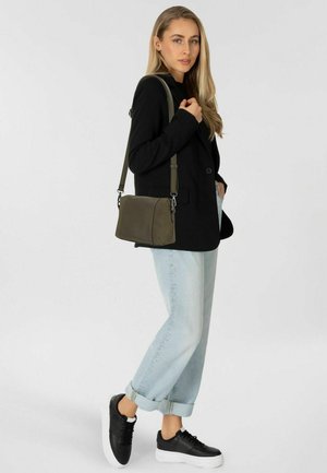 Schwarze Blazer, hellblaue Jeans mit hochgekrempelten Säumen, schwarze Sneakers mit weißer Sohle und eine kleine olivgrüne Umhängetasche mit verstellbarem Riemen.