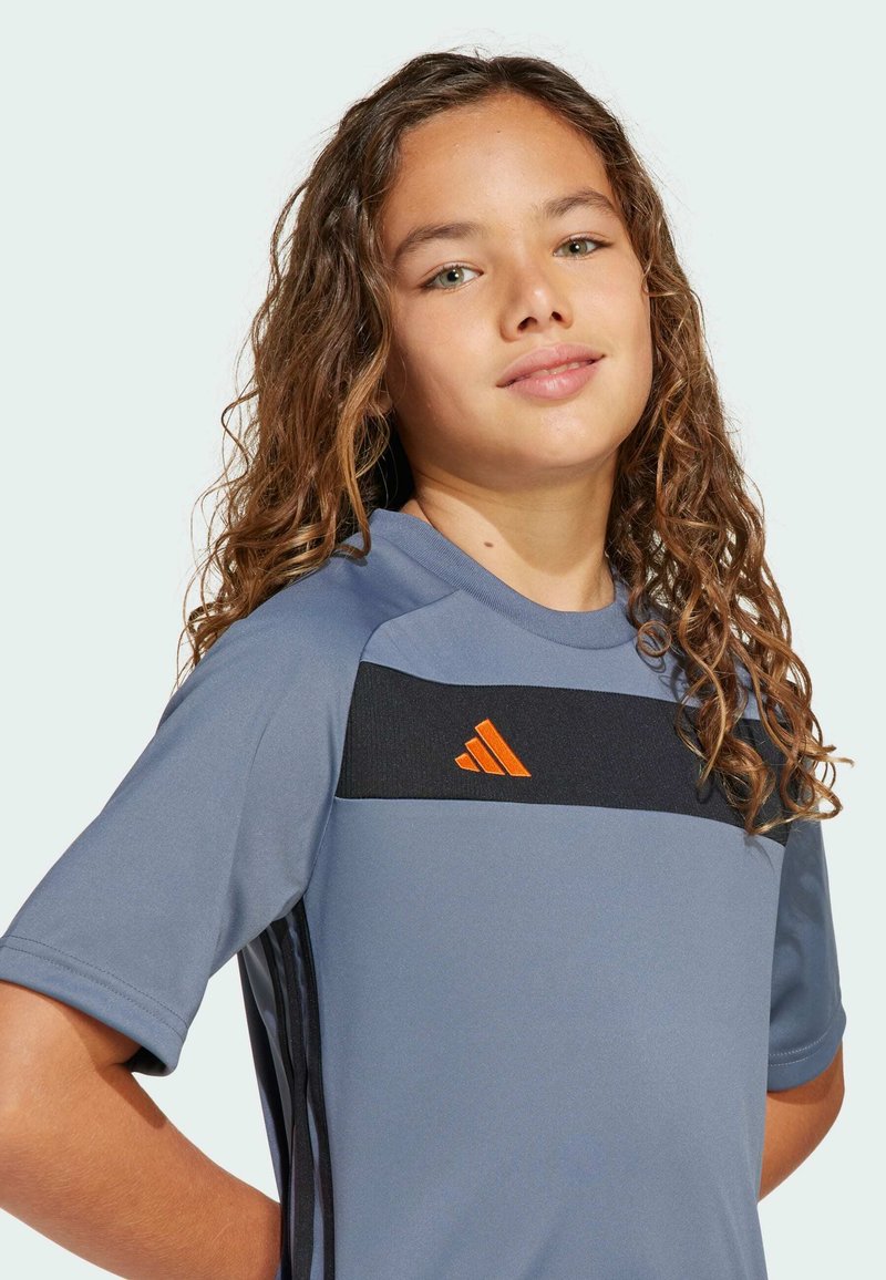 Grå träningsskjorta med korta ärmar, svart accentstripes och orange logotyp. Slät textur, designad för komfort och prestanda.