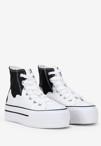 Zapatillas de lona de caña alta con un cuerpo blanco, acentos negros, cierre de cordones y una suela de plataforma con un diseño texturizado y una franja negra.