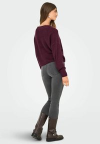 Bordo pleteni pulover s spuštenim ramenima, uparen s sivim uskim trapericama i smeškim čizmama do koljena koje imaju kopče i teksturirane potplate.