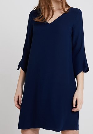 Granatowa sukienka z dekoltem w kształcie litery V, rękawami o długości do połowy ramienia z kokardami oraz luźnym krojem, wykonana z gładkiej tkaniny. Prosty i elegancki design.