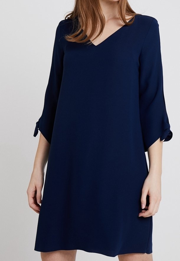 Robe bleu marine avec un col en V, des manches trois-quarts ornées de nœuds, et une coupe ample, confectionnée dans un tissu lisse. Design simple et élégant.