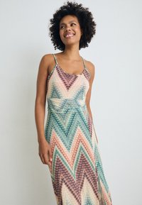 Maxi dress featuring a chevron pattern in pastel hues of pink, green, and blue. Thin straps and a knotted waist detail complete the design.