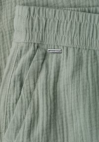 Light green textured fabric pants with elastic waistband and side pocket, featuring a small metal "Street One" brand tag.