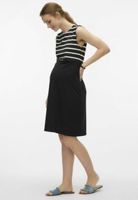 Maternity dress with a black skirt and a white striped top. Sleeveless design, soft fabric, knee-length, side pockets, paired with denim slide sandals.