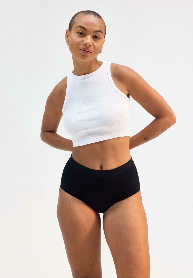 Vit ribbad crop-top som kombineras med högmidjade svarta underkläder. Toppen har en rund axelring; underkläderna har en slät midjeband och enkel design.