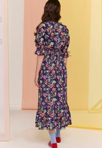 Sateen maxi dress in navy with puff sleeves, smocked waist, and layered ruffled hem. Decorated with colorful floral and leaf patterns.