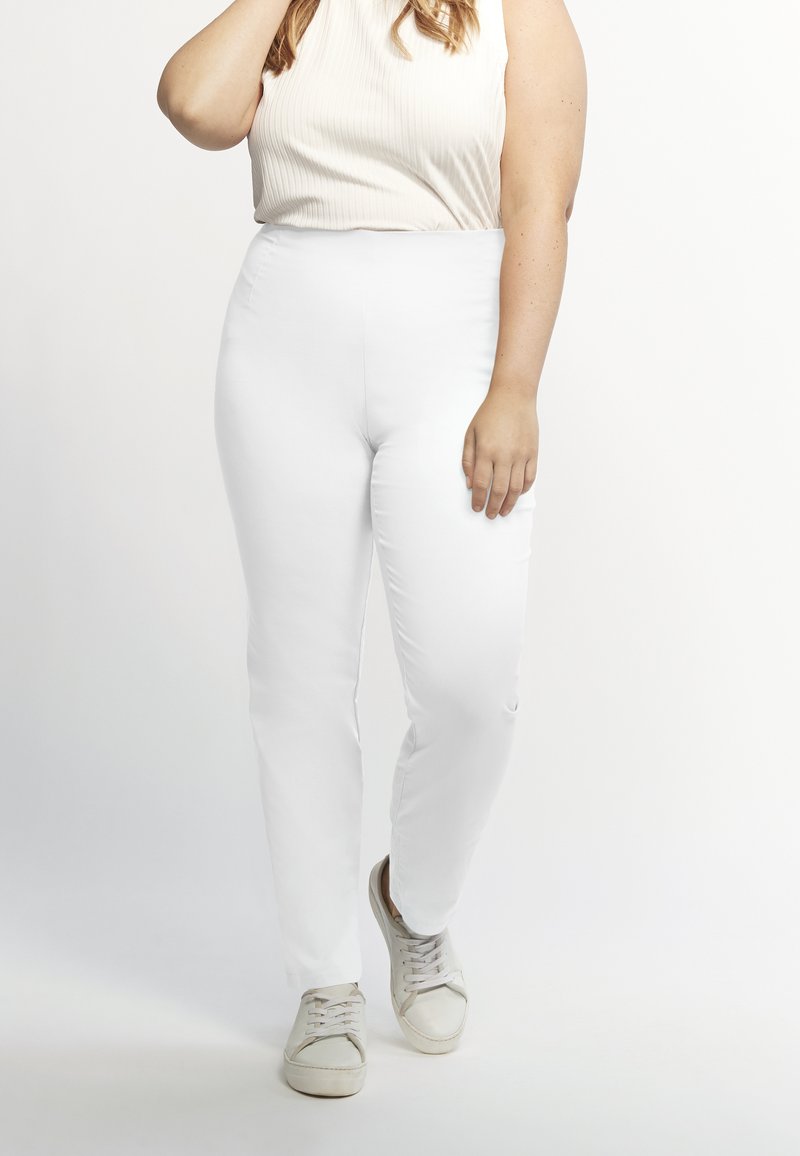 Witte slim-fit broek met een gladde textuur, hoge taille en een taps toelopend ontwerp, gecombineerd met lichtgrijze sneakers en een beige geribde top.