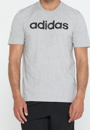 Camiseta de algodón gris con un gran logo negro de "adidas" en el pecho. Diseño clásico de cuello redondo y mangas cortas.
