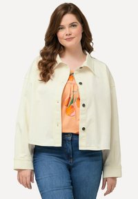 Lichtbeige cropped jack van textiel met structuur, voorzien van een reverskraag, knoopsluitingen en wijde mouwen, gedragen over een perzikkleurige blouse met een fruitprint.