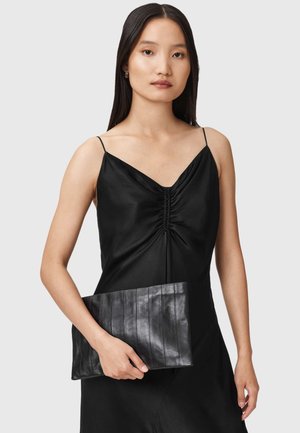 Zwarte leren clutch met een gestructureerd, verticaal streepend ontwerp vastgehouden in één hand. Vrouw draagt een zwarte satijnen jurk met dunne bandjes.