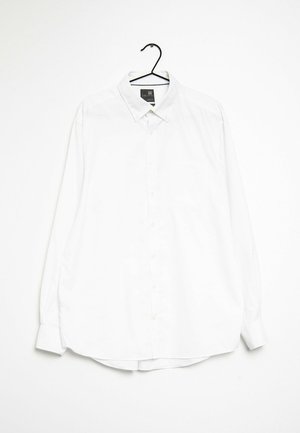 Camicia bianca a maniche lunghe con bottoni appesa a un appendiabiti nero. Presenta un colletto a punta, una tasca frontale e un tessuto morbido e liscio.