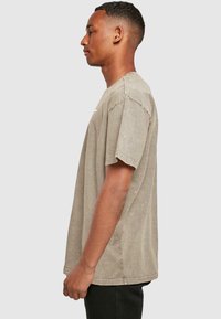 Šviesiai ruda trumpomis rankovėmis marškinėliai, laisvo silueto, pagaminti iš minkštos medžiagos, su apvalia iškirpte ir minimalia dekoracija priekyje.