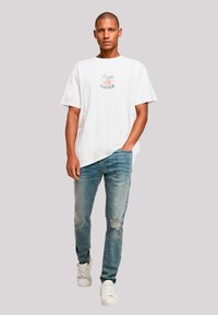 Witte katoenen t-shirt met de opdruk "Pasta Lover", gecombineerd met lichtblauwe versleten jeans en witte sneakers. Casual fit en korte mouwen.