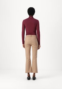 Bodysuit bordeaux à manches longues avec un col montant et un ruché à l'arrière, associé à un pantalon évasé beige. Chaussures noires visibles. Fond blanc.