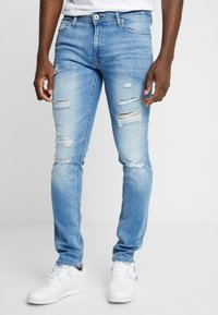 Ljusblå slitna denimjeans har flera revor, en slim fit och är kombinerade med vita sneakers för en avslappnad look.