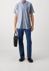 Korte mouwen, lichtblauw en wit gestreept overhemd met knopen, gecombineerd met blauwe spijkerbroek en zwarte schoenen, terwijl hij een zwarte tas vasthoudt.