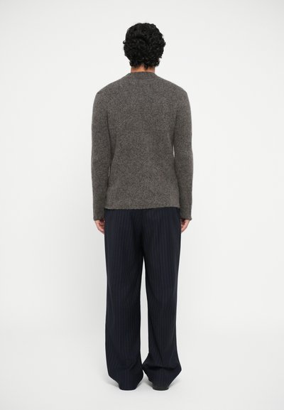 Brown knitted sweater with long sleeves, grayish texture, paired with loose-fitting dark striped trousers. Fabric appears soft and warm.