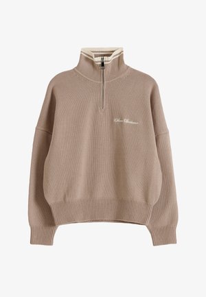 Béžový pletený pulovr s žebrovanými manžetami a lemem, límec na půl zipu s bílými proužky a malým kurzívním nápisem na levé straně hrudi.