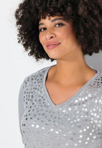 T-shirt gris en V avec un motif d'étoiles argentées sur un côté ; texture douce, coupe décontractée et manches courtes.