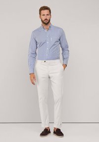 Camicia a righe blu e bianche con bottoni, pantaloni bianchi slim-fit e mocassini scuri. Tessuto morbido, design su misura e orli dei pantaloni arrotolati.