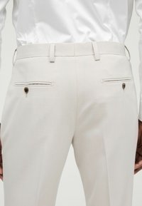 Pantalones tailored de color beige claro con ajuste slim, que cuentan con dos bolsillos traseros con cierres de botón y pasadores para cinturón para un ajuste ajustable.