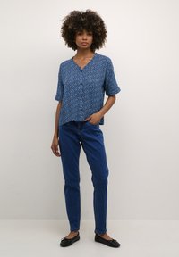 Mėlyna gėlėta marškinė su mygtukais, trumpomis rankovėmis, deranti su priglundančiais tamsiai mėlynais džinsais ir juodais plokščiais bateliais. Paprasta, laisva išvaizda.