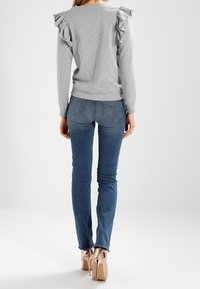 Vaaleanharmaa collegepaita röyhelöityillä olkapääkoristeilla, yhdistettynä sinisiin kapeisiin farkkuihin ja beigen värisiin korokepohjakenkiin. Tasainen tekstiilipinta.