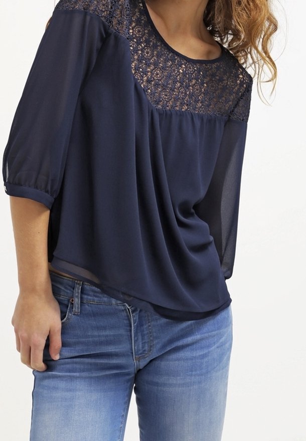 Blusa blu navy con dettagli in pizzo sulla parte superiore anteriore e maniche trasparenti, caratterizzata da una vestibilità comoda e scollatura rotonda, abbinata a jeans.