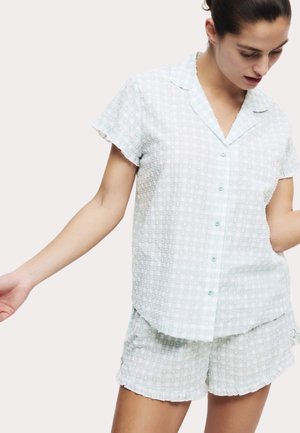 Short-sleeve, button-up pajama set in light green checkered pattern. Soft, textured fabric with ruffled edges on sleeves and shorts.