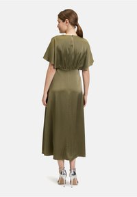 Olivengrünes Midi-Kleid mit Flatterärmeln, geraffter Taille, Rückenverschluss und eleganten, silbernen High-Heels. Glatte, glänzende Textur.