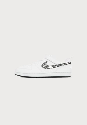 Hvid lavtop sneakers med sort-hvid zebrastribet Nike-logo og velcrolukning på ensartet lys baggrund.