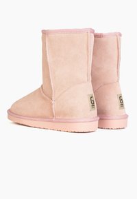 Botines de ante rosa con punta redondeada, suela acolchada y costuras cosidas. Presentan un parche de logo en el lateral y forro de textil suave.