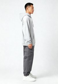 Felpa grigia con tasca a canguro, vestibilità rilassata, cappuccio con cordino; abbinata a pantaloni cargo grigi scuri e sneakers bianche.